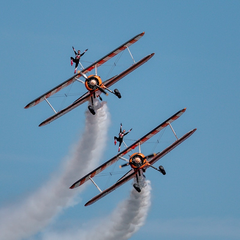 Two wing walkers performing on two biplanes flying in the sky
